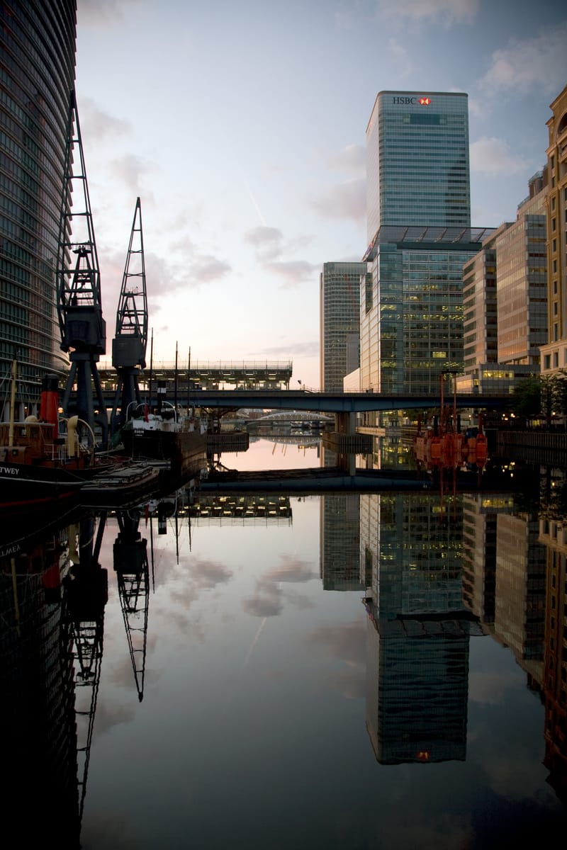 Dock cranes and Canary Wharf towers reflected in calm water at sunrise