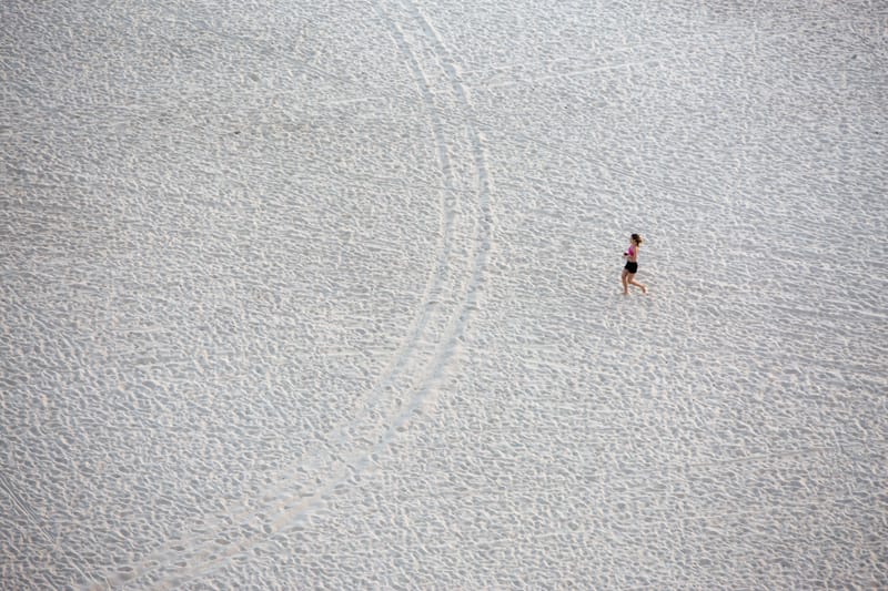 A lone runner crossing a vast expanse of pale sand, seen from above — Ipanema Beach, Rio de Janeiro