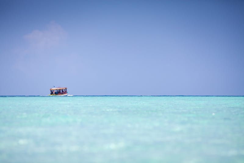 Small boat crossing a flat turquoise sea under a hazy sky, Maldives